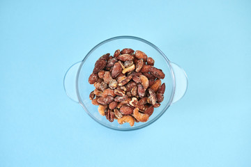 A glass bowl with nuts, isolated on light blue background, shot from the above.