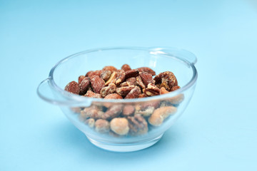 A glass bowl with nuts, isolated on light blue background. Nutritious vegetarian food snack.