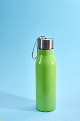 Bright green sport bottle for water with silver metallic lid and grey strap, isolated on light blue background. Healthy lifestyle concept.