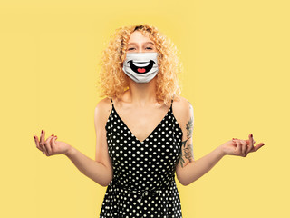 Happy laugh. Portrait of young caucasian woman with emotion on her protective face mask isolated on studio background. Beautiful female model. Human emotions, facial expression, sales, ad concept.