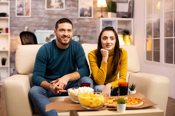 Beautiful young couple watching TV and eating fast food takeaway