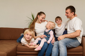 Young parents and three children playing on sofa and fool around. Happy big family concept