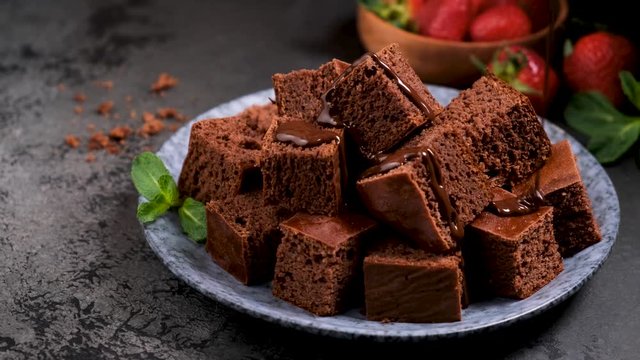 Chocolate sauce pouring on chocolate brownie cakes. Homemade dark chocolate cake cut in squares on black background