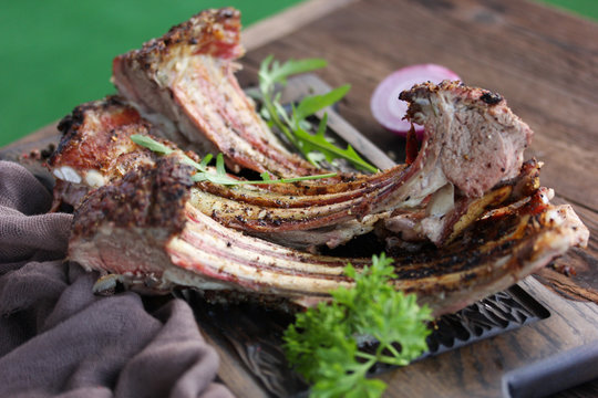 Roast rack of lamb with parsley, arugula and onion rings on a dark wooden board. Summer, barbecue, meat ribs. Background image, copy space