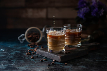 Ice coffee espresso a glasses, with milk, being poured over from pitcher by hand. Summer refreshing beverage.