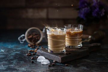 Splash of iced coffee in a glass glass and coffee beans on a brown background. Summer refreshing...