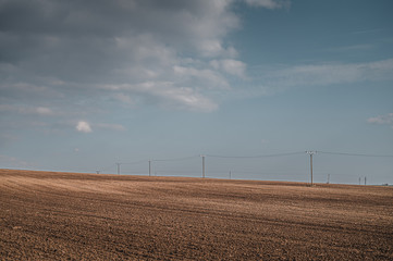 Spring field landscape. Blue sky with white clouds in background. Freshly plowed fields and electric poles.