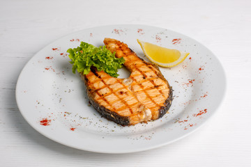 Grilled salmon steak served with lemon on a white plate