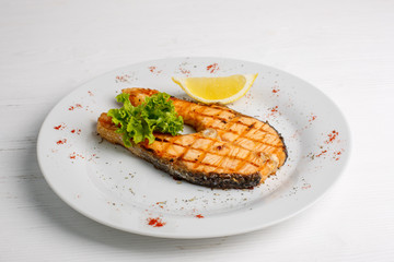 Grilled salmon steak served with lemon on a white plate