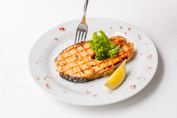 Grilled salmon steak served with lemon on a white plate