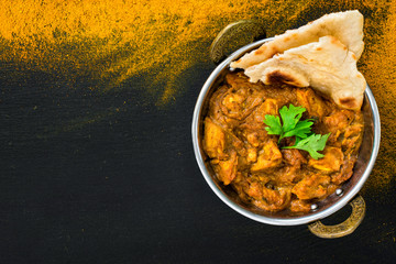 Chicken tikka masala spicy curry meat food served in karhai or kadhai and fresh naan bread on black stone background