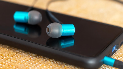 Headphones lie on a black smartphone, listening to music