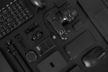 Flat lay of black office desk table with many black gadgets - obrazy, fototapety, plakaty