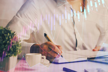 Double exposure of man's hands writing notes of stock market with forex chart.