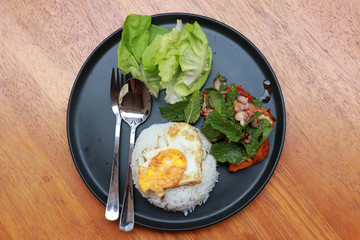 Breakfast in the black round plate on the wooden floor. Fried egg rice and blend of fried chicken with lettuce.