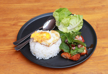 Breakfast in the black round plate on the wooden floor. Fried egg rice and blend of fried chicken with lettuce.
