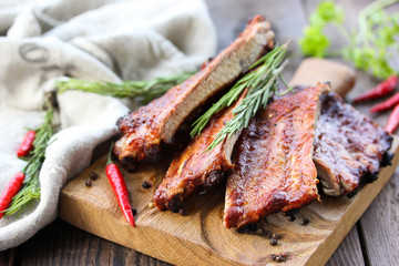 Fried pork ribs with a fried crust with spices, rosemary, parsley and chili pepper on a wooden board on a brown wooden background with fork. Rustic. Meat on grill. Background image, copy space