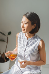 Pretty young woman with tasty cookie and cup of tea at home