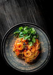 Stir fry noodles with vegetables and shrimps in plate on black wooden table background