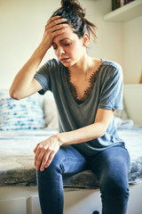 Woman suffering from knee pain while sitting on bed.