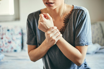 Woman suffering from joint pain while sitting on bed.
