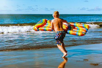 Boy on the beach. Beach holidays and sports. A boy with a colored air mattress runs into the sea
