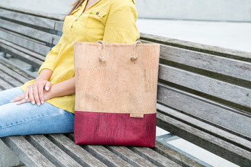 Close up of young woman sitting on wooden bench in city with her eco friendly cork tote bag from...