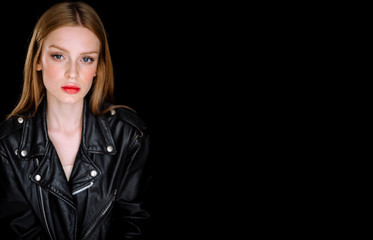 Portrait of a model girl in a black biker leather jacket. young woman with brown hair posing on black background