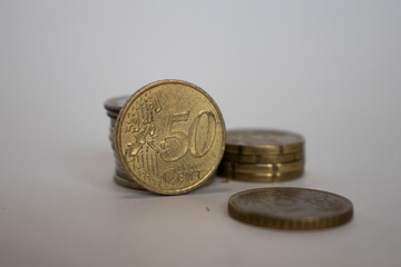 a coin worth fifty euro cents stands upright next to the other coins lying one on one on a white background.