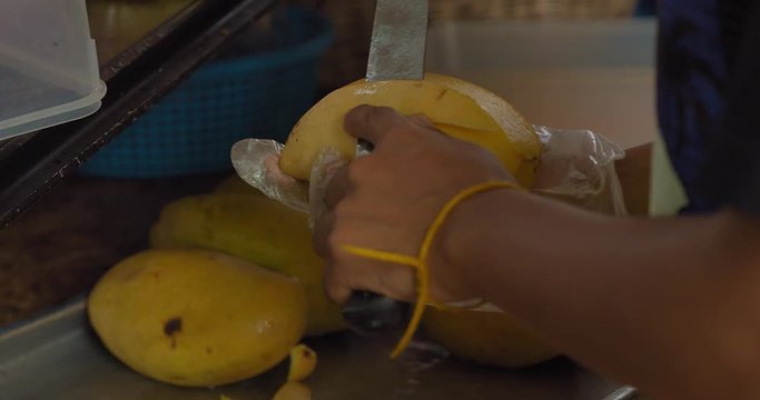 Girl hands; She is using a sharp knife to clean yellow mango. Video made at Phuket, Thailand.