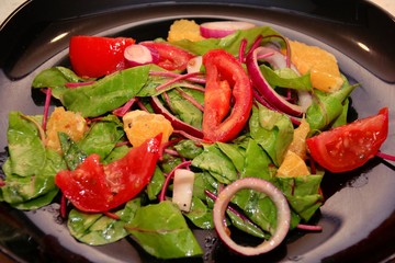 Orange and tomato salad with red onions and new beet leaves on a black plate