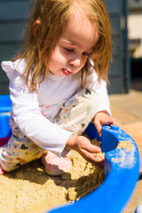 Baby girl playing in a sandbox outdoors in sunny day. Child in blue sandbox in summer.