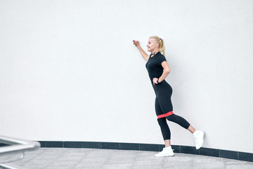 Crossfit healthy lifestyle concept. Young sporty woman doing exercises with red fitness rubber outdoor on white wall background.