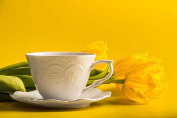 Yellow tulips with cup of tea or coffee on yellow