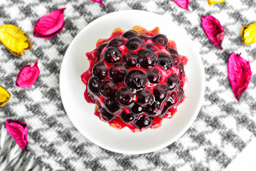 Fruit cake with currant covered with jelly on a saucer on a beautiful background