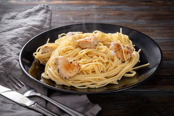 pasta , spaghetti with chicken fillet on a black plate on a dark wooden , napkin, fork,