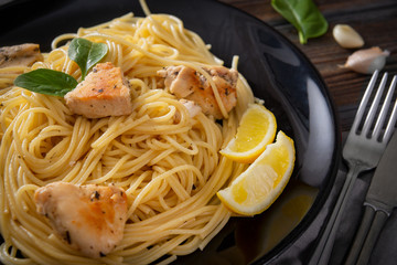 spaghetti , pasta  with chicken fillet, lemon slices, tomato, garlic, on a  plate on a dark ,  closeup