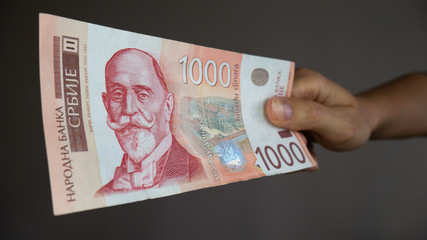 The hand gives money - Serbian 1000 dinar currency banknote. Serbia money RSD dinar cash, portrait of Dorde Vajfert.