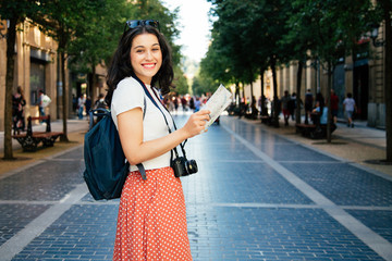 Happy young tourist woman exploring the city with a map