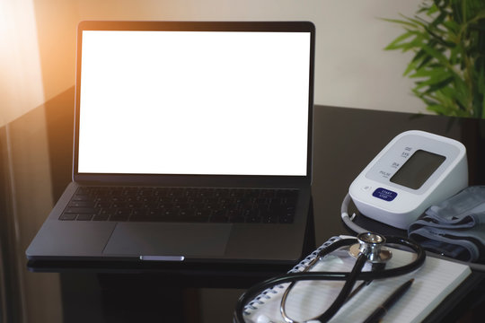 Mockup image of laptop computer with blank white screen, medical stethoscope, sphygmomanometer and notebook on dark mirror desk. e health, telehealth, telemedicine or online medical concept.
