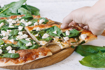 Pizza with spinach on a white background. Diet Pizza. Proper nutrition. Hand takes pizza