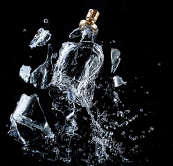 A glass perfume bottle shatters on a black background with splashes and drops of water - 336377032
