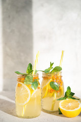 A jar of homemade lemonade with lemon, berries and mint on a light background, sunlight