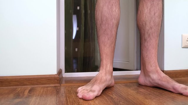 Frumpy man with hairy legs in shorts barefoot crosses the threshold, enters the balcony of a Flat. Dolly Shot, Moving Camera.