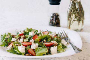 Light spring salad on a white background. Proper nutrition. Diet. Proper nutrition. Diet. Slat with greens, strawberries and cheese