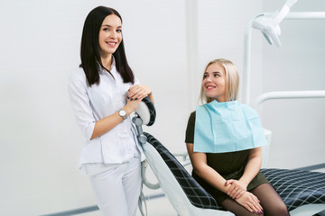 Obraz premium Portrait of a friendly smiling female dentist with happy patient in the office of a modern dental clinic.