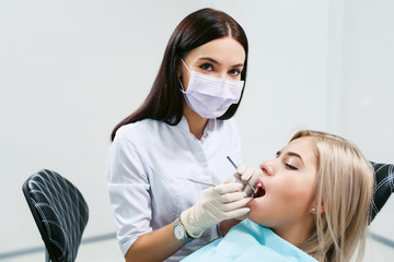 Dentist examining a patient's teeth in modern dentistry office. Closeup cropped picture with copyspace. Doctor in disposable medical facial mask.