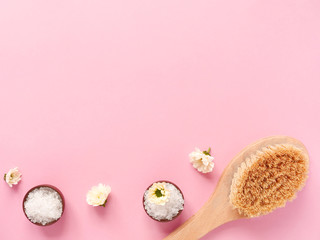 Spa flatlay composition. Sea salt in jars, massage wooden brush, flower on pink background. Copyspace, top view. Home care concept, relax and rest