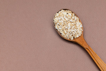 oat flakes in a wooden spoon on a brown background