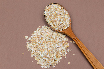 oat flakes in a wooden spoon on a brown background